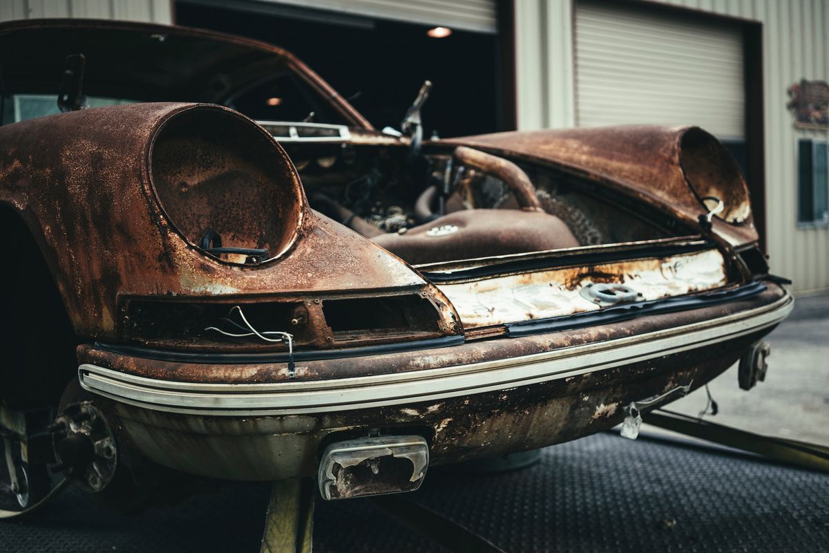 Derelict, rust-covered Porsche 911/912 front clip, stripped for restoration. Shows pitted bodywork & original bumper trim.