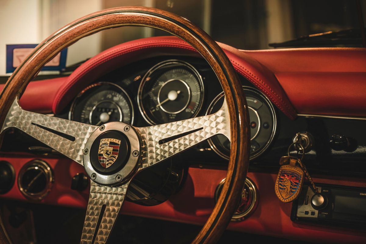Vintage Porsche 356 interior with wood-rimmed steering wheel, engine-turned spokes, Porsche crest, red leather dash.