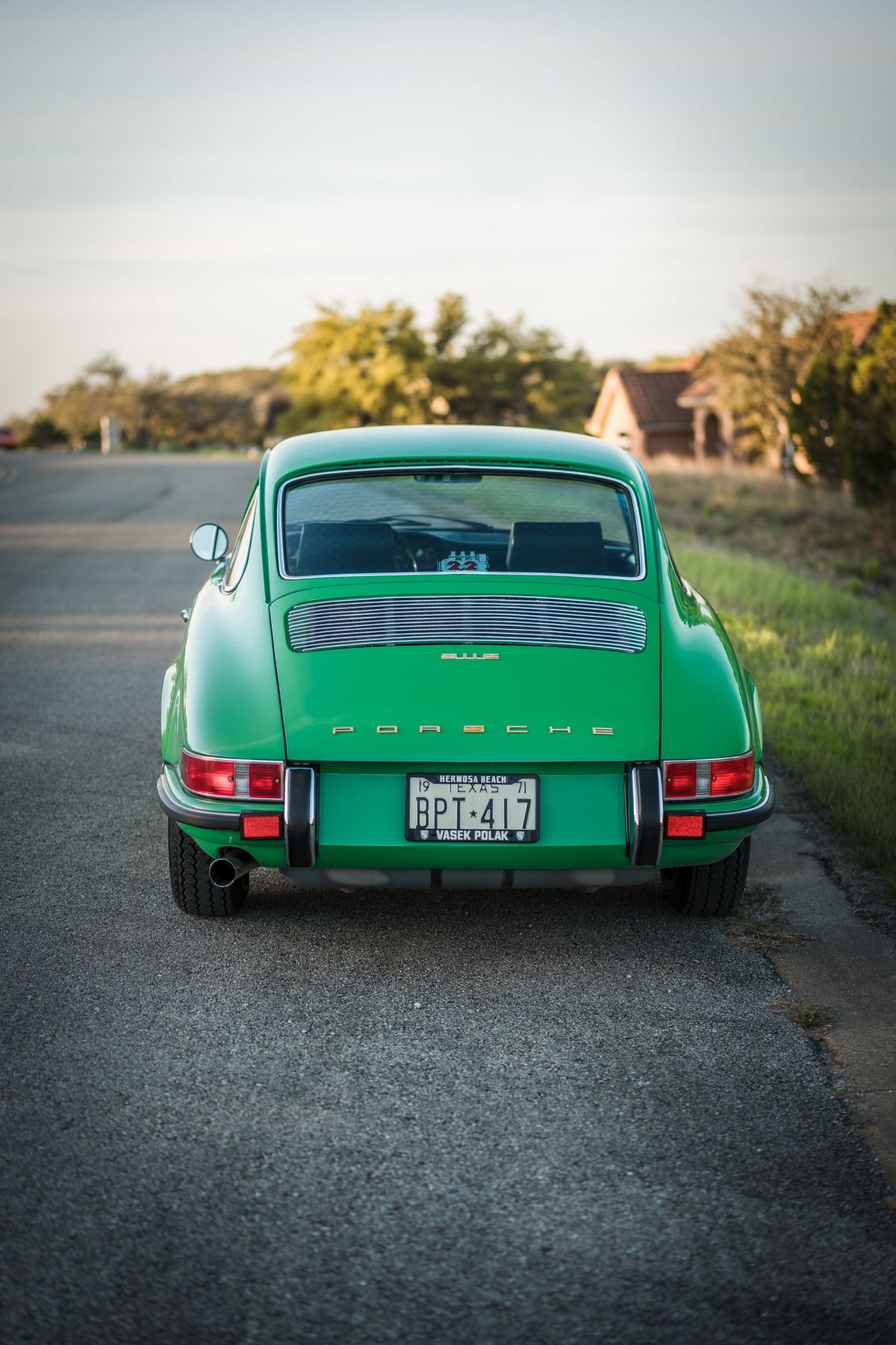 Rear of a Conda Green 1971 Porsche 911E. Features chrome "PORSCHE" script, slatted engine grille, bumperettes, and Texas plate.