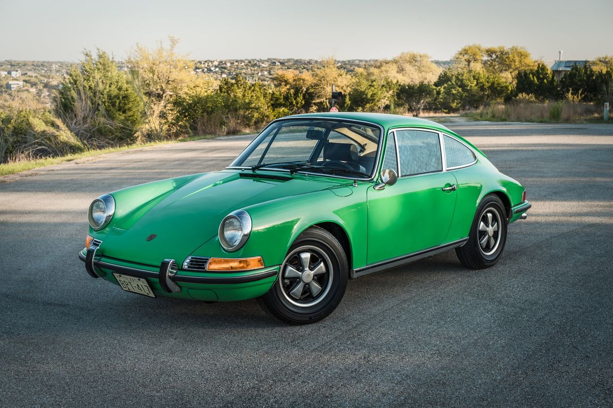 Vibrant Conda Green 1971 Porsche 911E coupe with polished chrome trim and iconic Fuchs rims, parked outdoors.