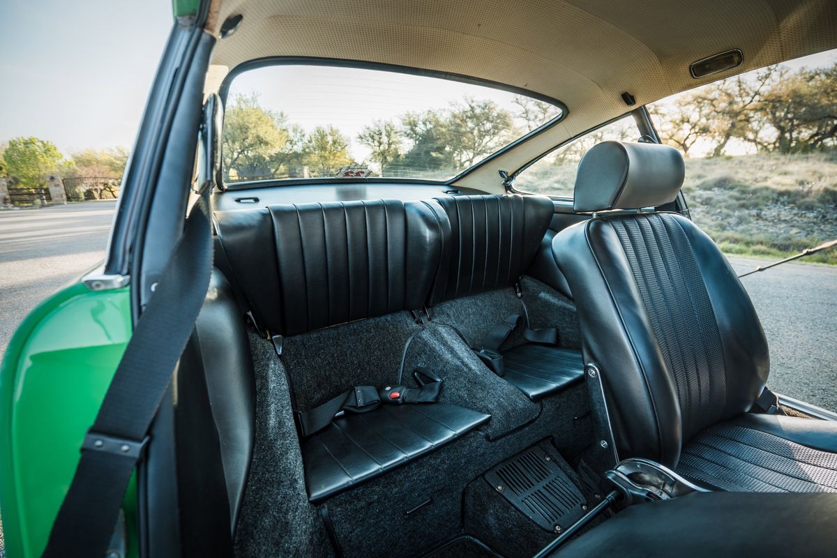 Interior view of a Conda Green 1971 Porsche 911E, featuring black leather seats, dark grey carpet, and a perforated headliner.