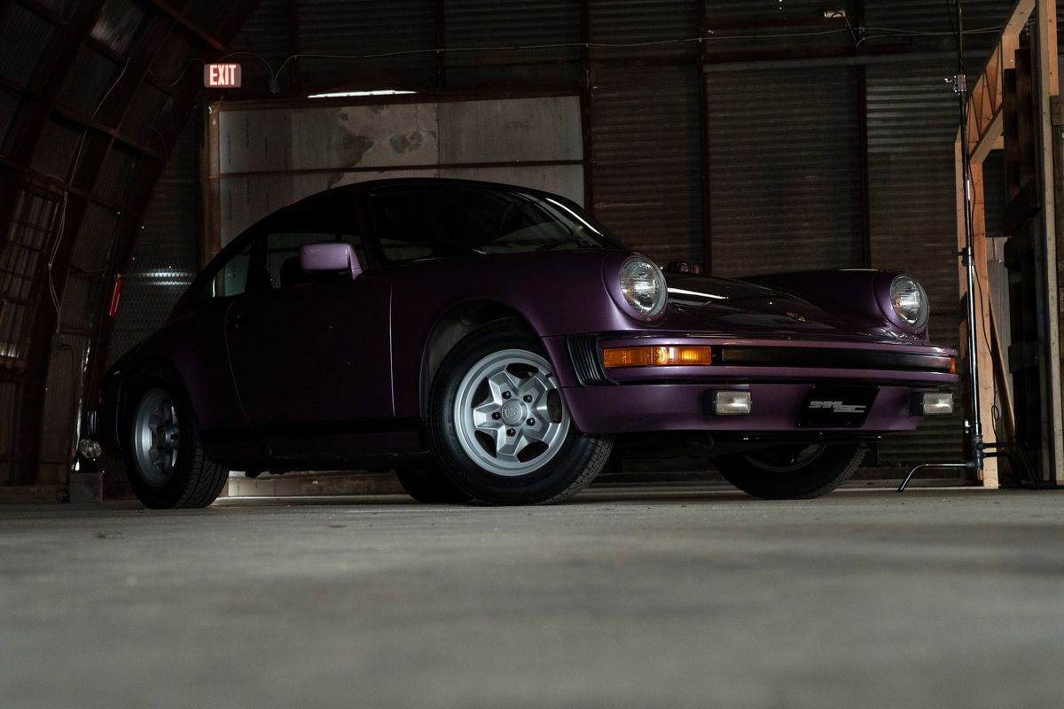 Metallic purple Porsche 911SC coupe, front quarter view, with silver Fuchs rims and black trim, inside a dark industrial garage.