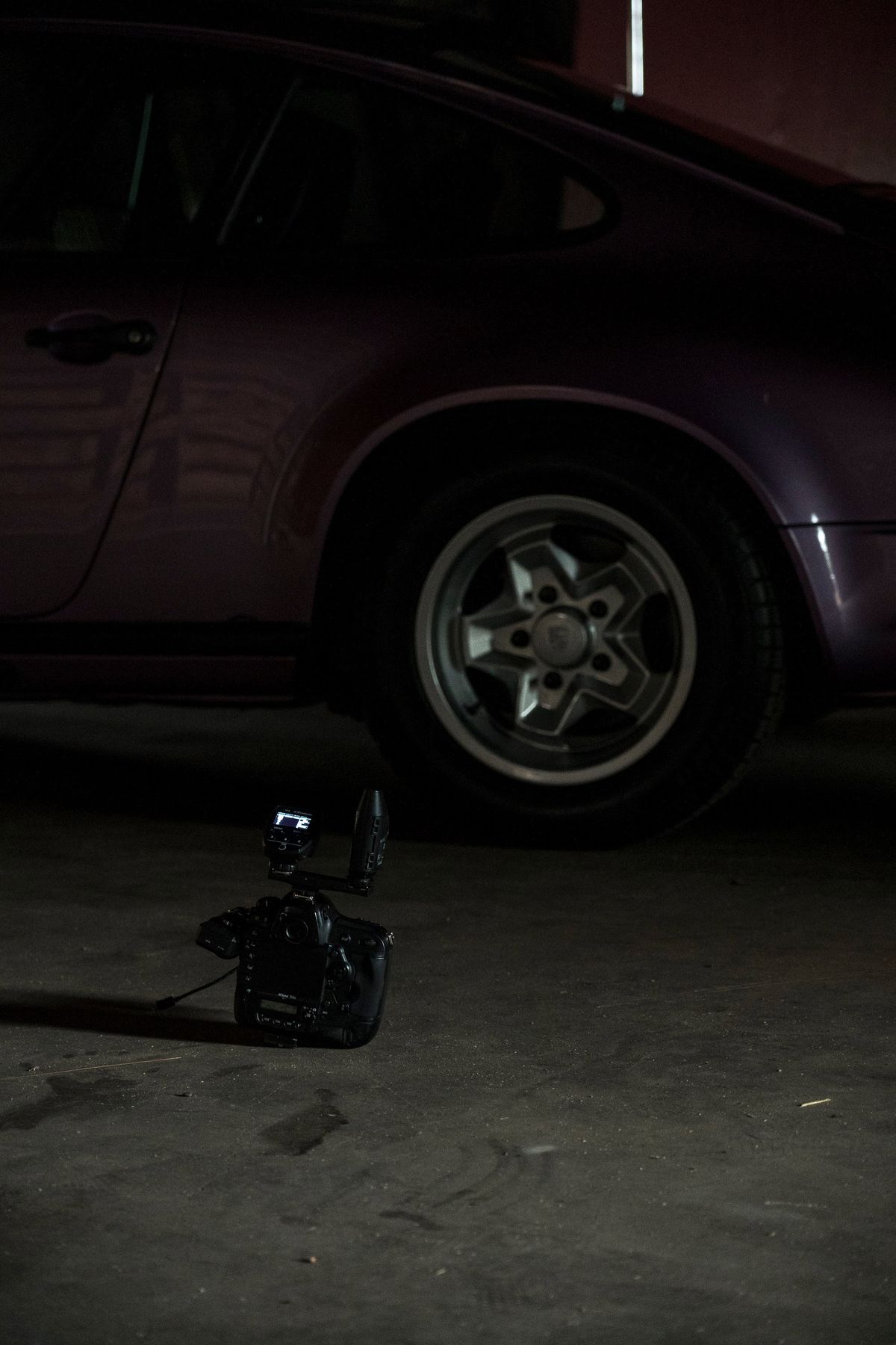 Close-up of a vintage purple Porsche 911's rear quarter panel, featuring iconic Fuchs-style wheels in low light.