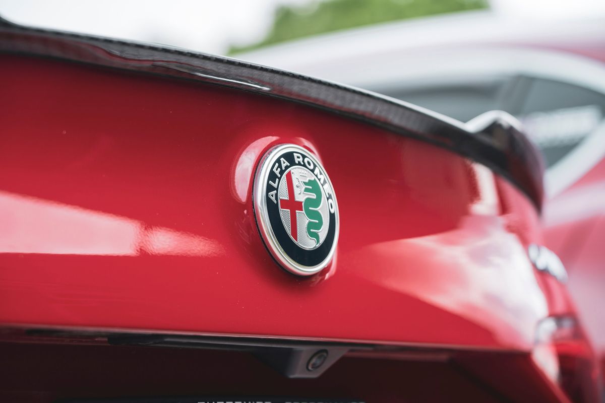 Red Alfa Romeo Giulia Quadrifoglio rear trunk with iconic emblem, carbon fiber spoiler, and rearview camera.