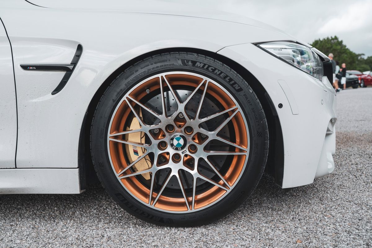White BMW M4 coupe showcasing Frozen Gold multi-spoke M Performance wheels, Michelin PS4S tires, and large gold M brake calipers.