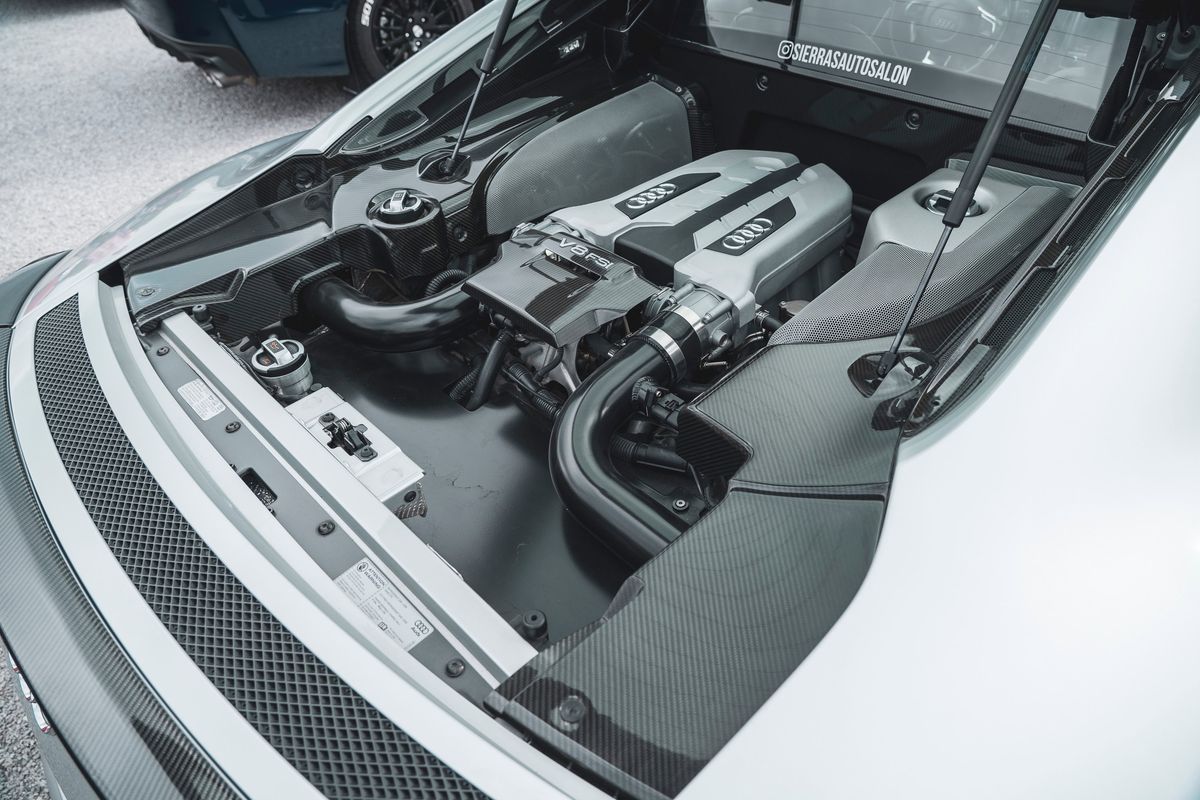 Overhead view of a white Audi R8 V8 FSI mid-engine, featuring carbon fiber trim panels & exposed engine bay components.