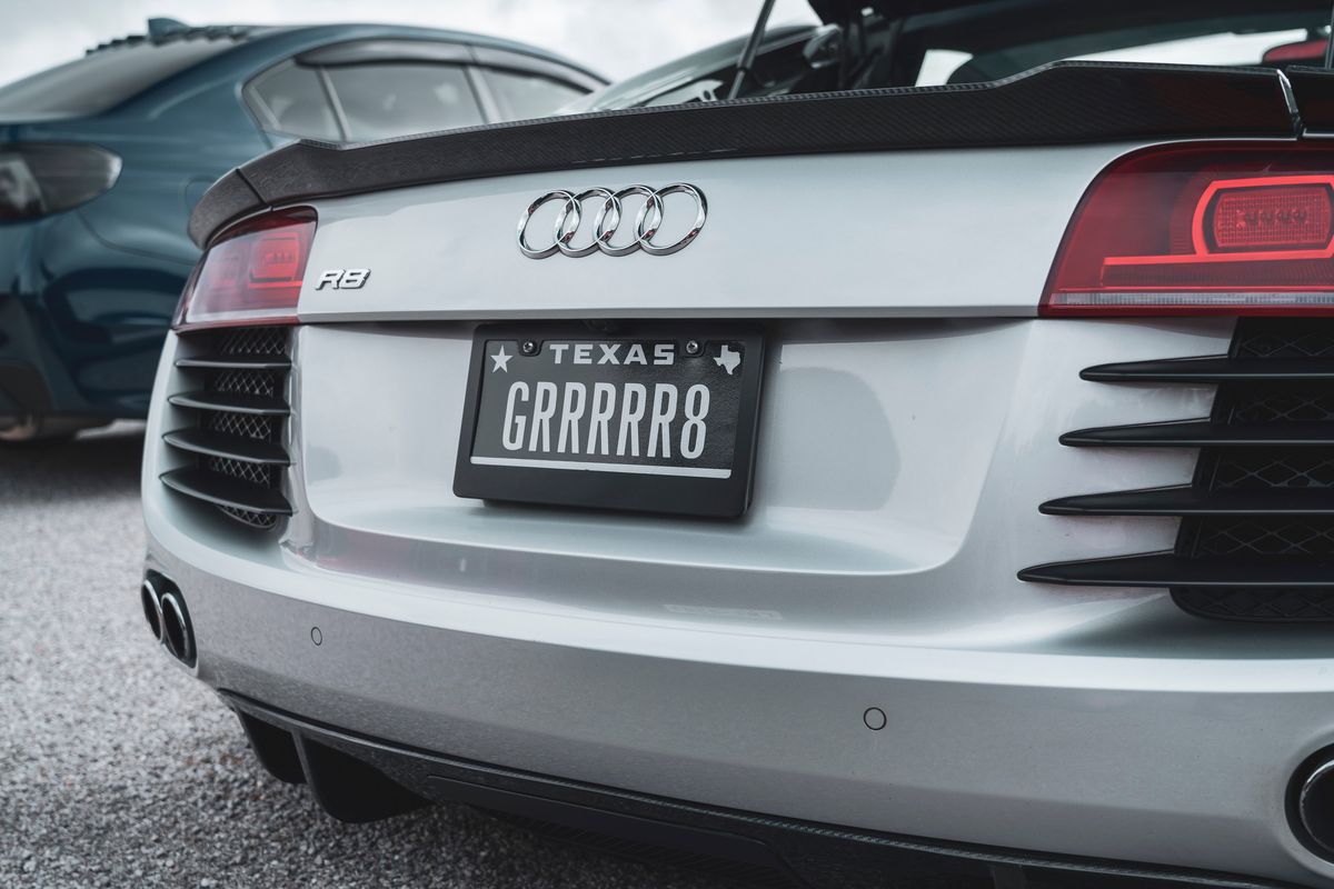 Silver Audi R8 rear showcasing a carbon fiber spoiler, signature LED taillights, aggressive bumper vents, and a Texas GRRRRR8 plate.