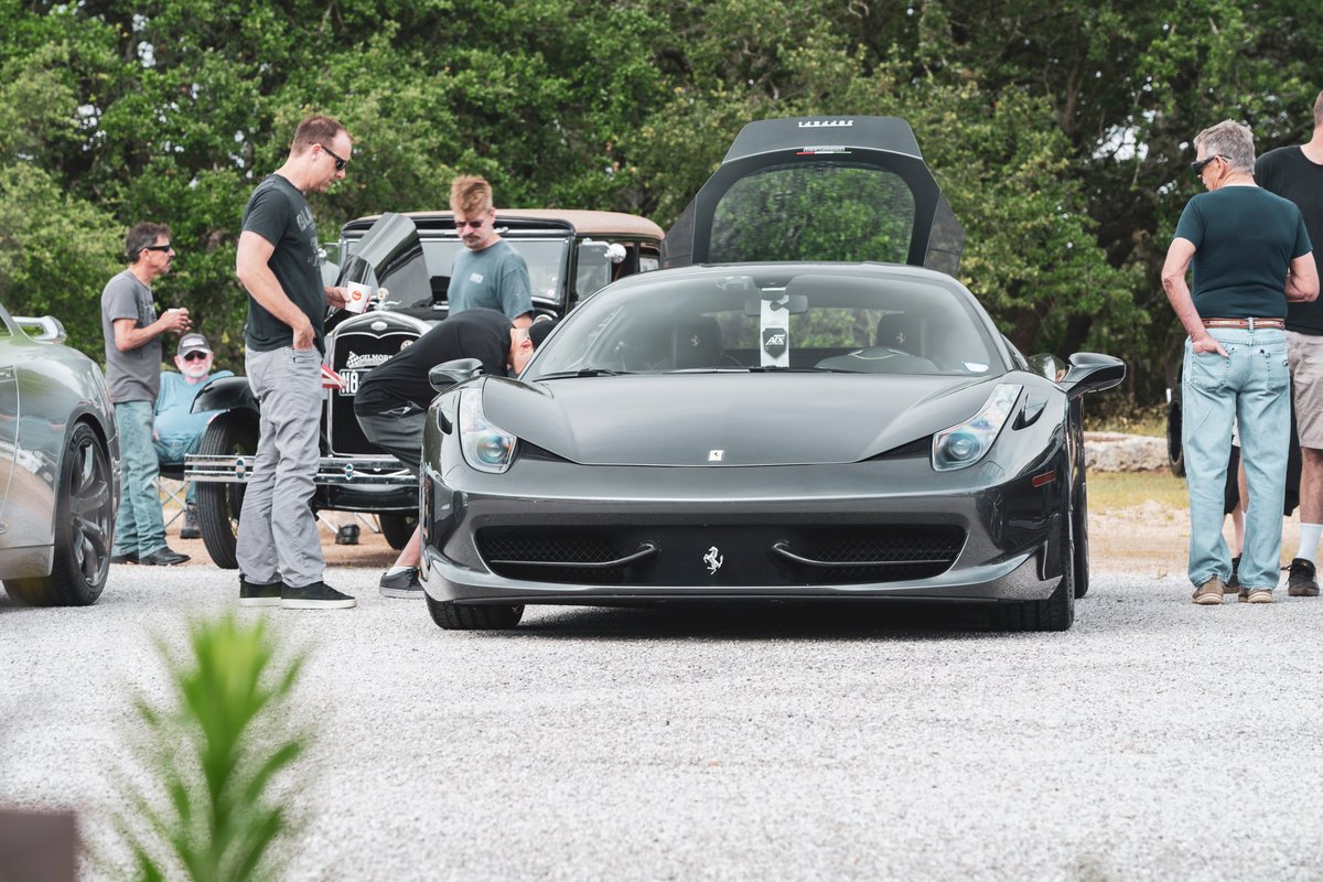 Front view, dark grey Ferrari 458 Italia at Coffee & Cars Dripping Springs. Open rear engine cover, visible Ferrari trim, front tow hook.