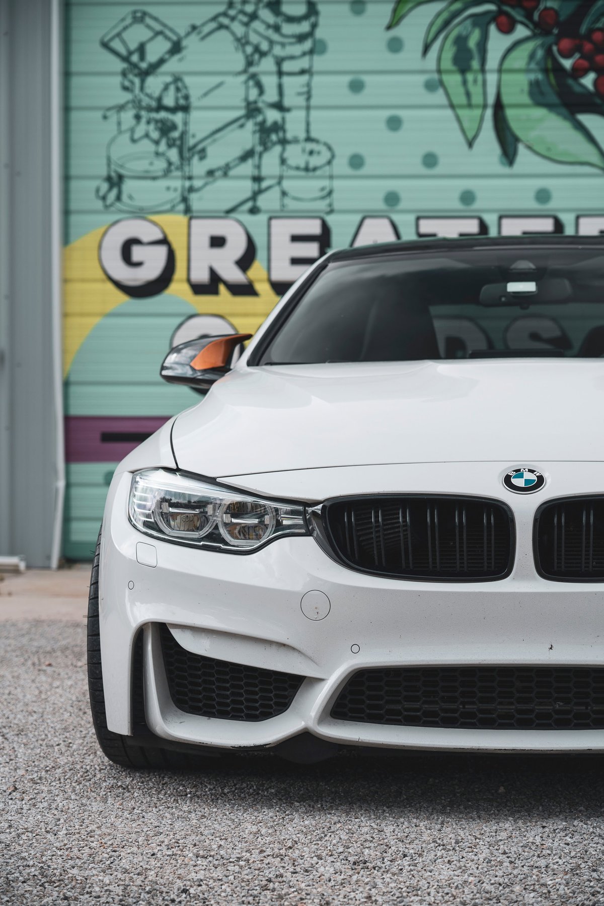 Front end of an Alpine White BMW M4 coupe featuring black M-kidney grilles, LED headlights, & M-sport aero.