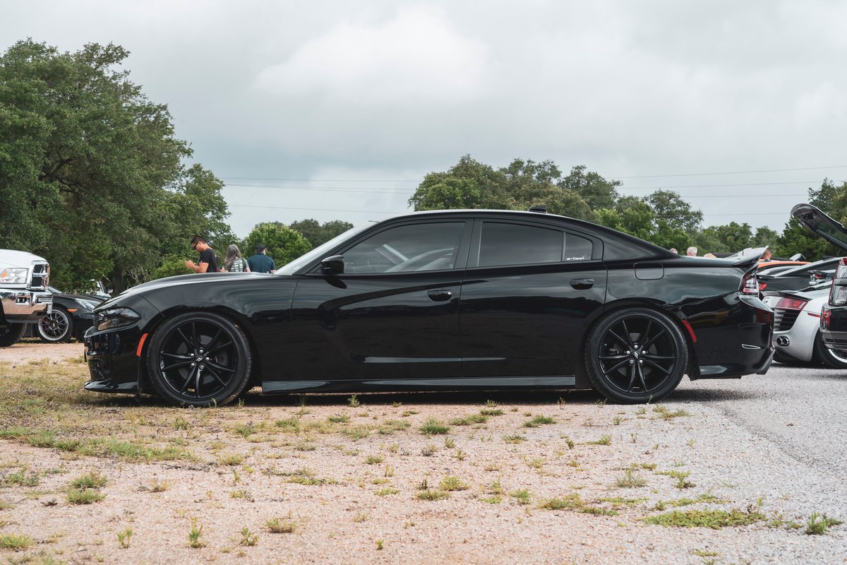 Black Dodge Charger sedan with black multi-spoke rims and lowered stance, parked at a Coffee & Cars event.