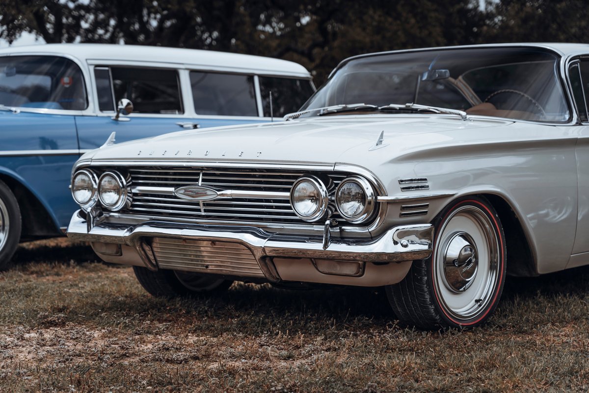 Front view of a classic light cream 1961 Chevrolet Impala sedan, featuring quad headlights, chrome grille, and redline tires on white rims.