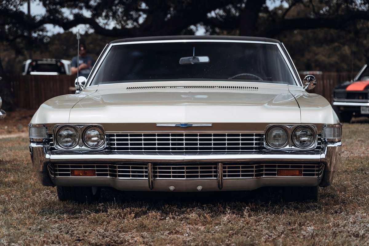Gold 1967 Chevrolet Impala front view, featuring stacked quad headlights, prominent chrome grille, and black vinyl roof.