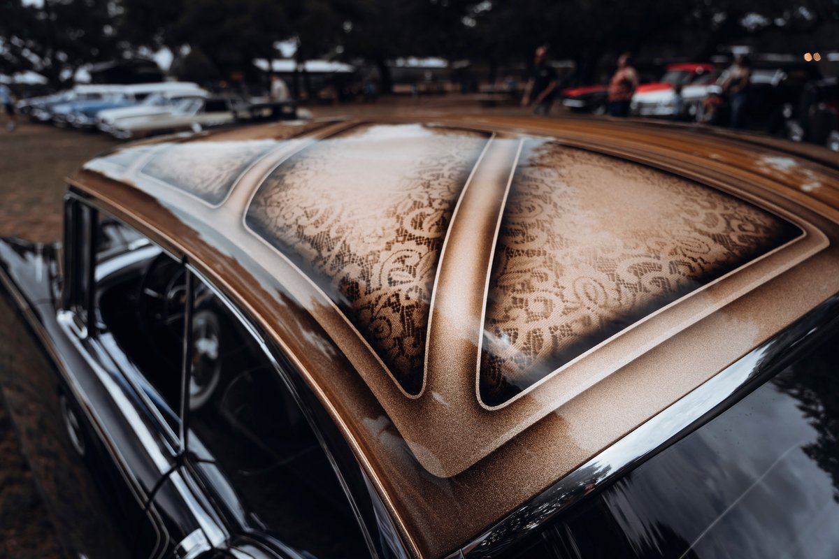 Classic car with bespoke roof livery: intricate tan lace pattern, metallic bronze flake panels, dark body, chrome trim details.