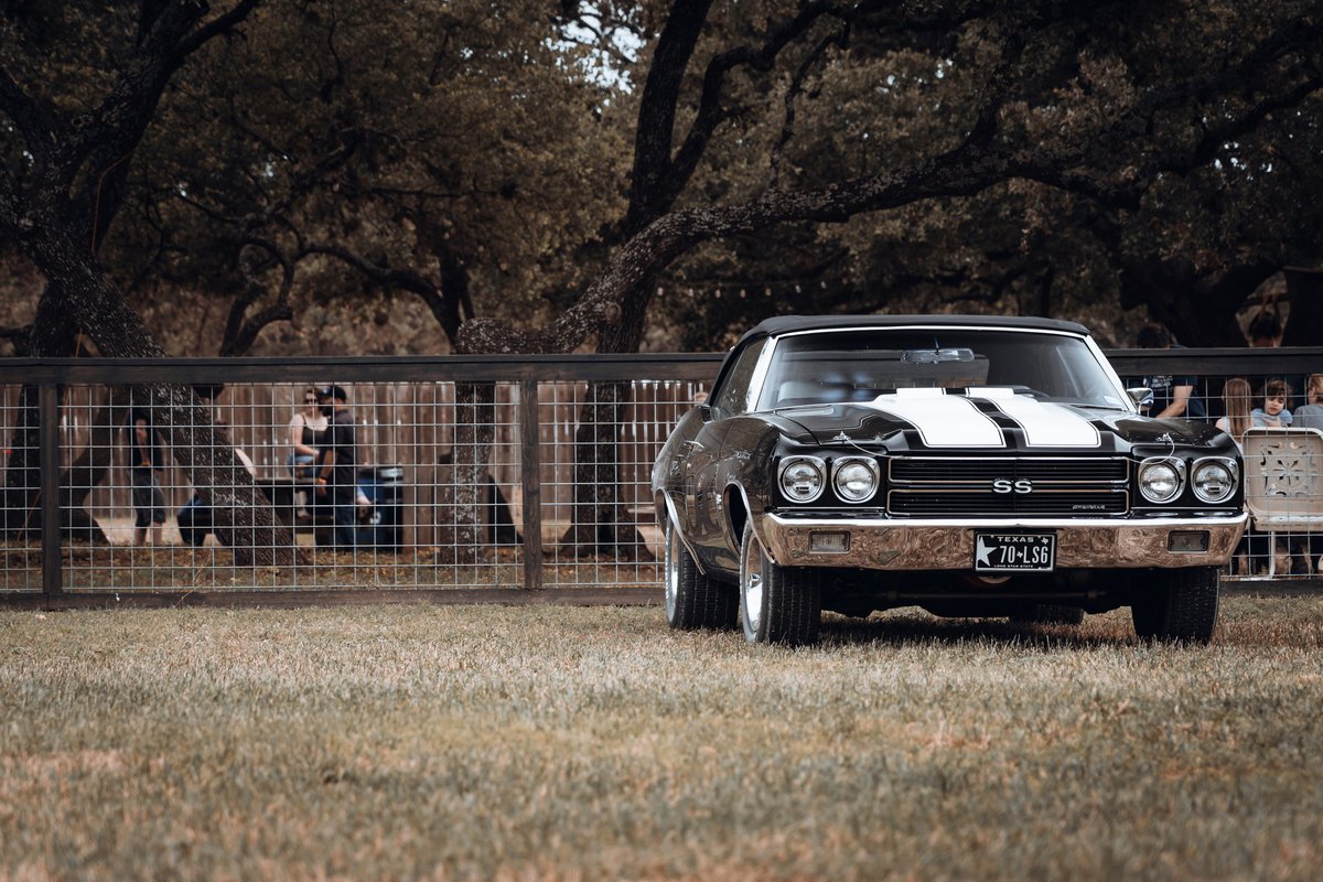 Black 1970 Chevrolet Chevelle SS LS6 convertible with white racing stripes, chrome trim, and rally wheels parked on grass.