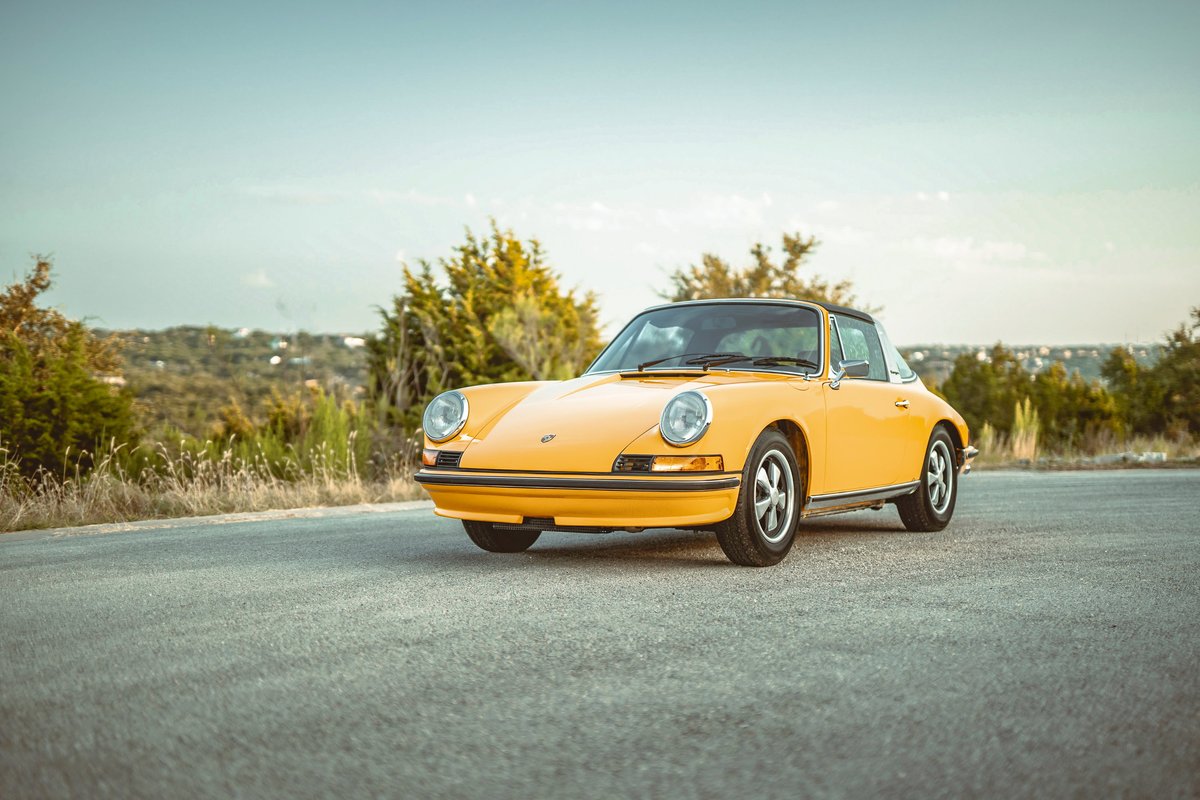 Front 3/4 view of a Signal Yellow 1973 Porsche 911S Targa with classic Fuchs rims, parked outdoors.