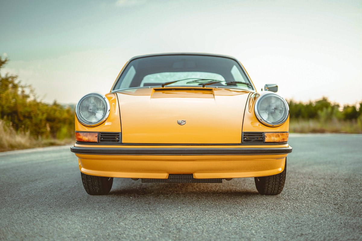 Iconic Signal Yellow 1973 Porsche 911S, front view showcasing its classic round headlights and black bumper trim.