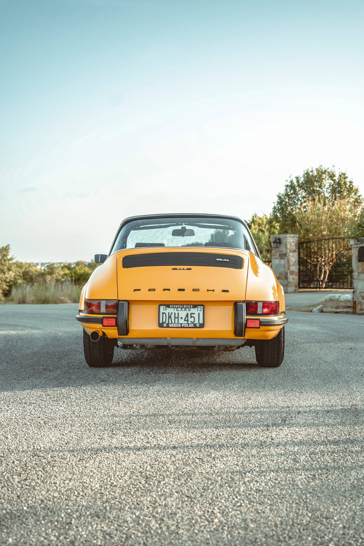 Rear view of a vibrant Signal Yellow 1973 Porsche 911S Targa. Features classic black bumperettes, single exhaust, and 'PORSCHE' script.