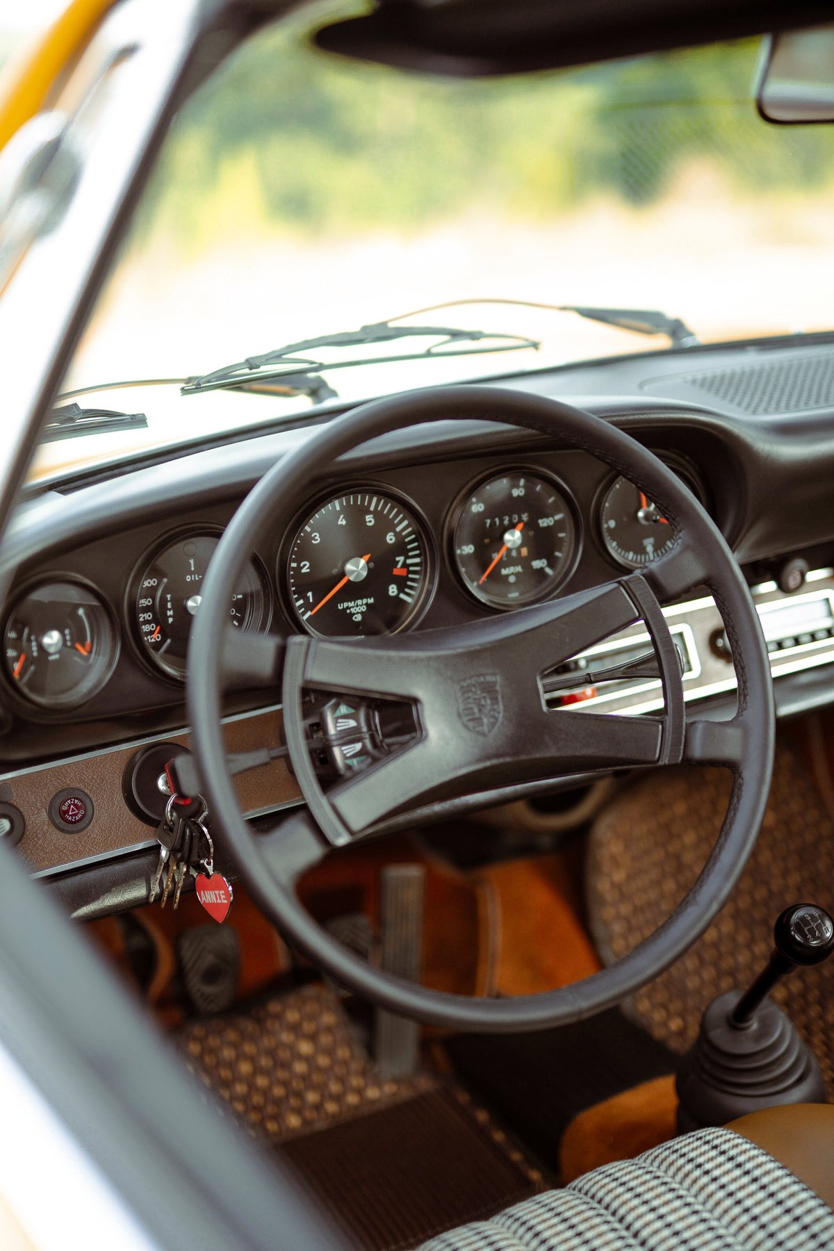 1973 Signal Yellow Porsche 911S interior: black steering wheel, classic five-dial dash, manual shifter, Pepita seat trim.