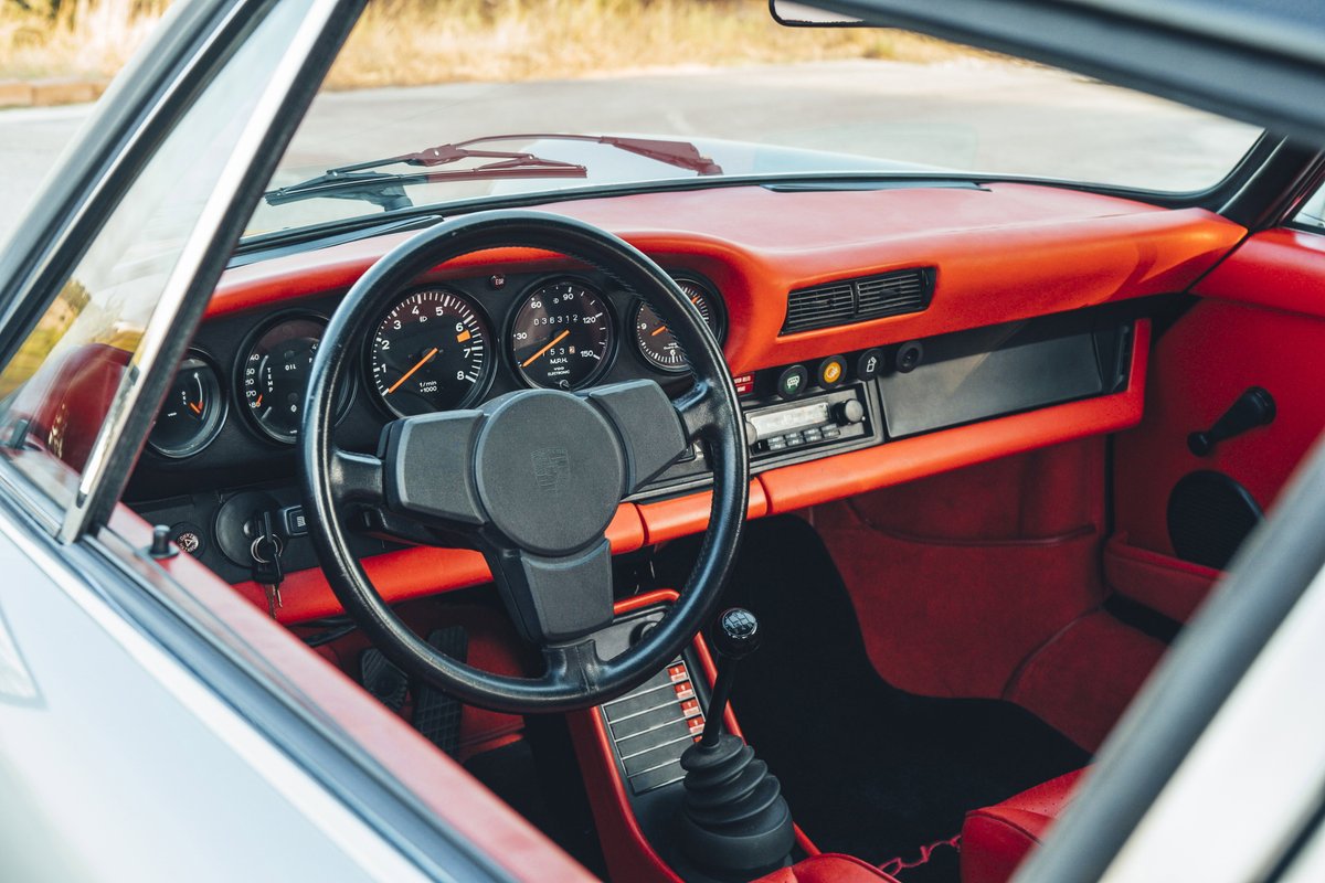 1977 Porsche 911S interior with bold red trim, classic five-dial gauge cluster, black steering wheel, and vintage stereo.