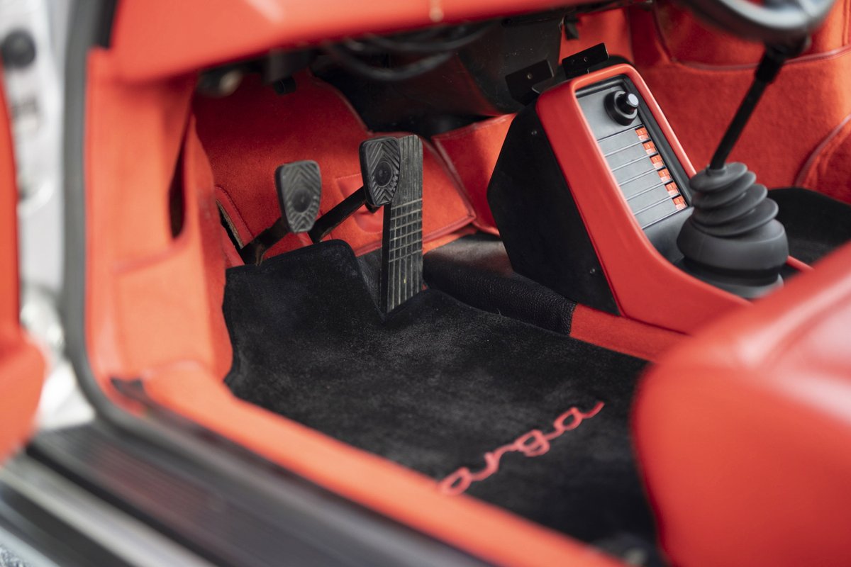 1977 Porsche 911S Targa interior: vibrant red trim, black 'targa' floor mats, manual shifter & ribbed performance pedals.