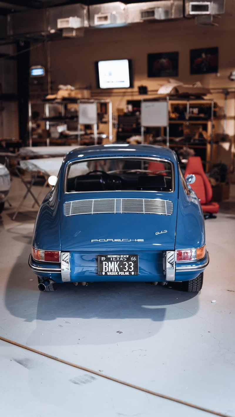 Pristine blue 1966 Porsche 911 2.0 SWB, rear view in a workshop, showcasing its engine grille and classic chrome trim.