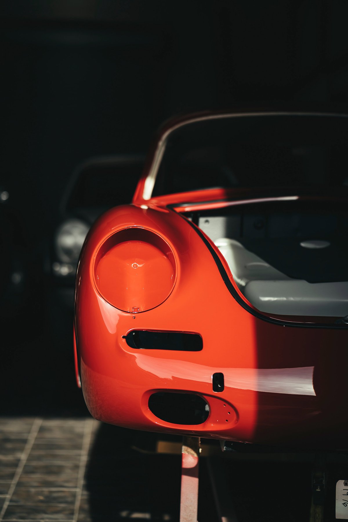 Close-up of a brilliant red Porsche 356 front fender & headlight recess during restoration, highlighting glossy paint & trim openings.