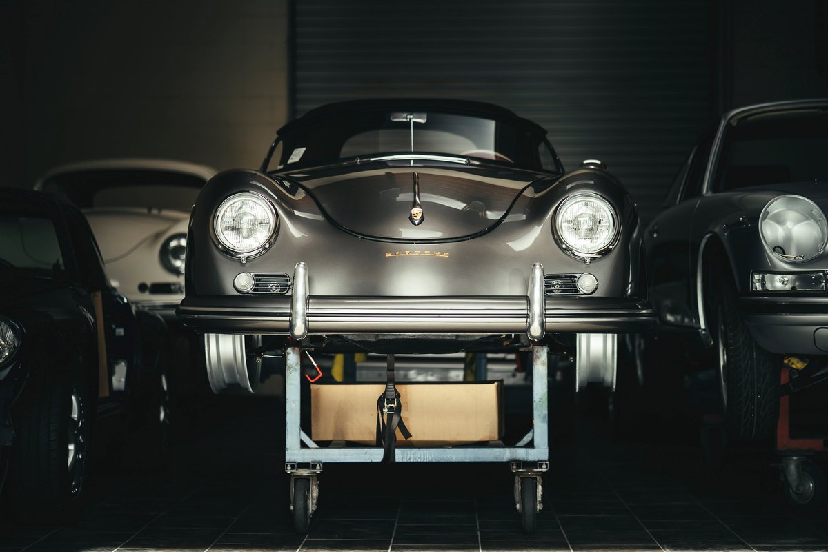 Gunmetal grey Porsche 356 coupe on a workshop dolly, featuring elegant chrome bumperettes and classic round headlights.
