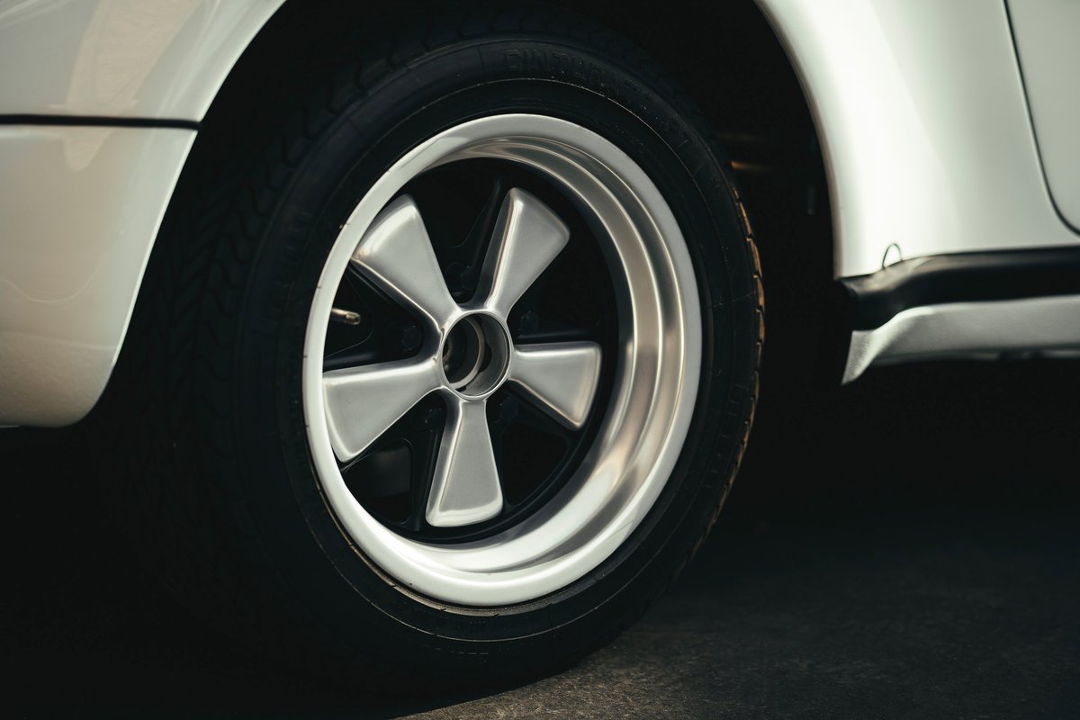 White classic air-cooled Porsche 911 with polished Fuchs 5-spoke alloy wheels, black centers, and black rocker trim.