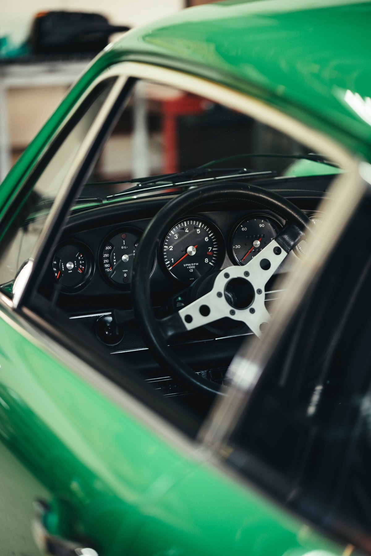 Green classic Porsche 911 interior at Lit Show LA, featuring its black 5-dial gauges and drilled racing steering wheel.