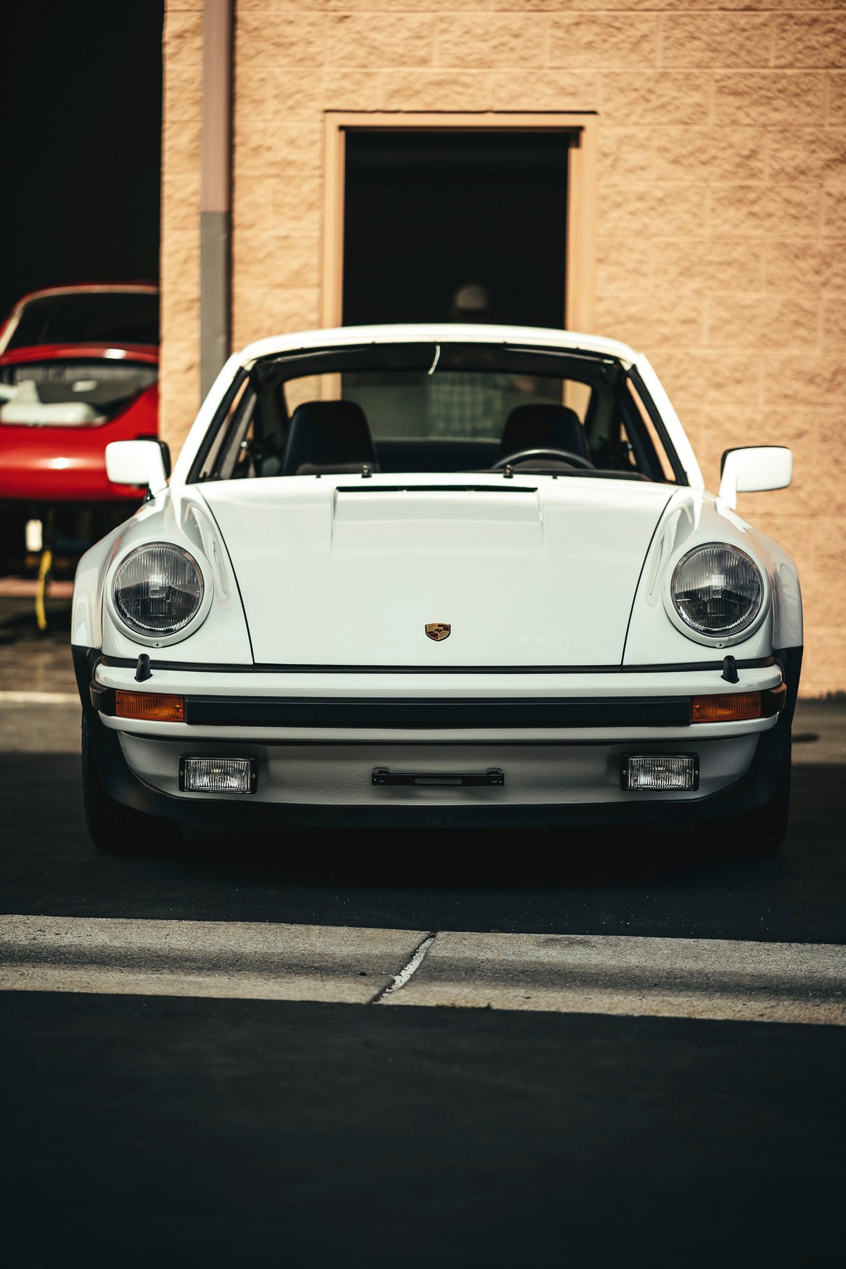 Frontal view of a pristine white classic Porsche 911 G-series with iconic round headlamps and black impact bumpers.