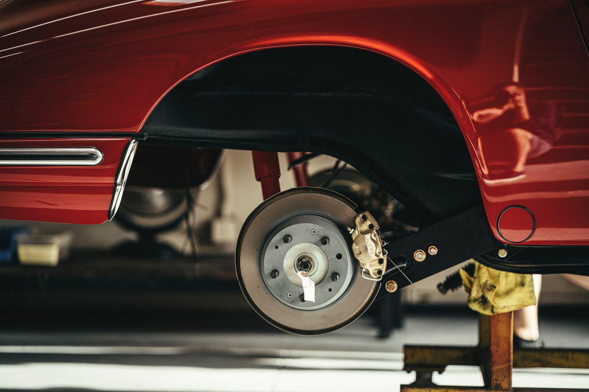 Red classic air-cooled Porsche 911 with exposed brake rotor, gold caliper, and suspension in the rear wheel arch.