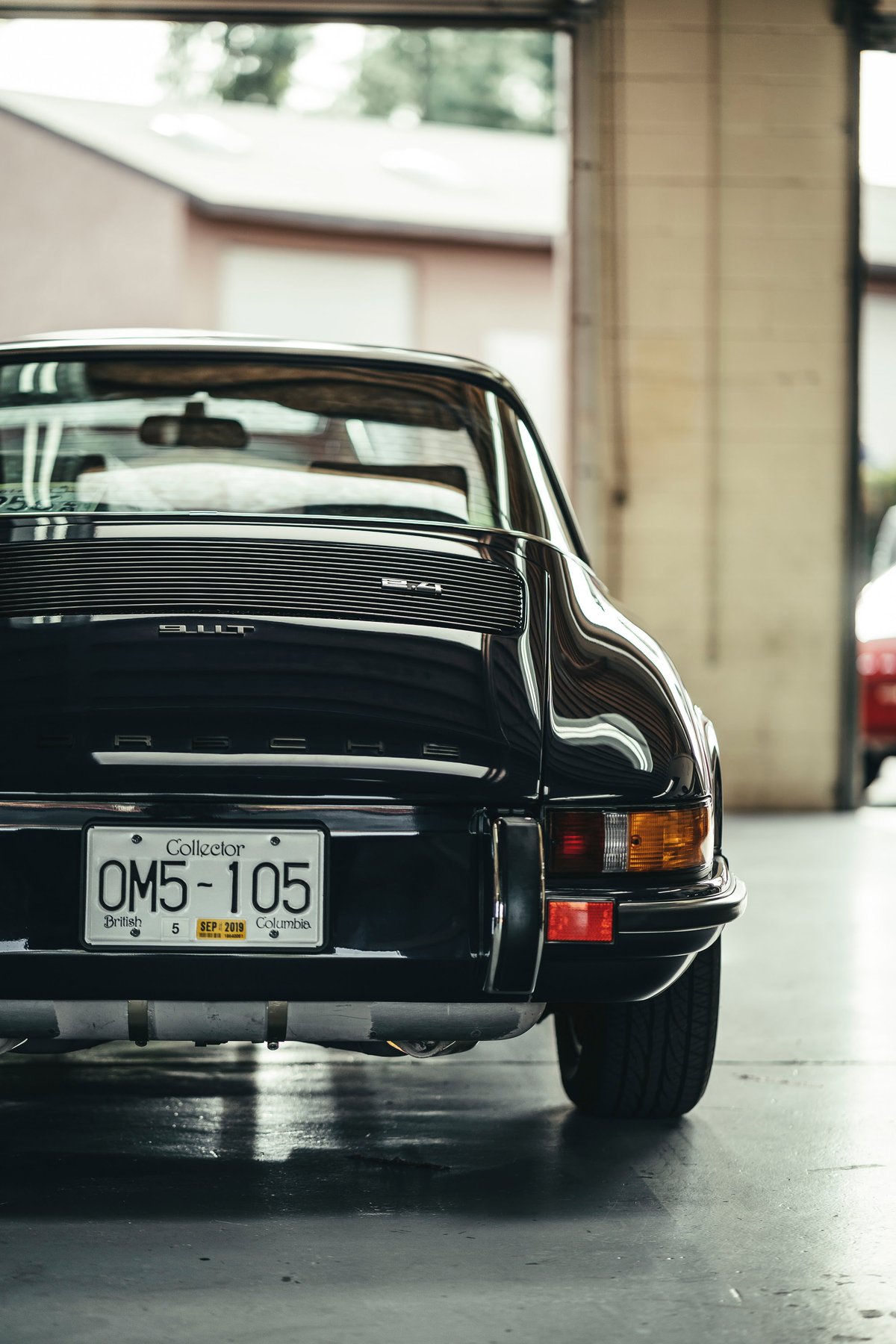 Rear view of a black classic Porsche 911T sports car. Features horizontal decklid grille, chrome bumper trim, and Collector plate.