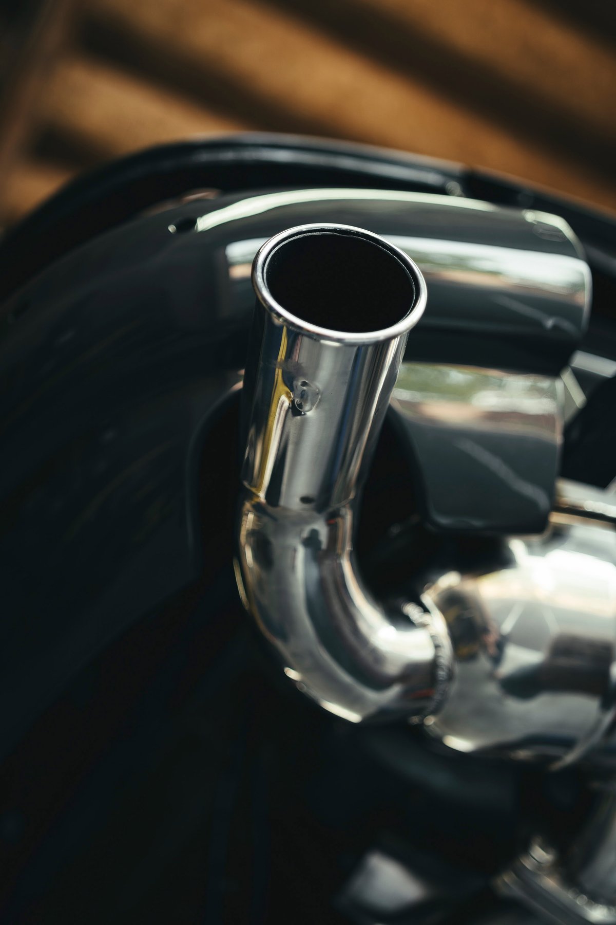 Polished chrome single exhaust tip of a classic deep black Jaguar E-Type. Visible welds and pristine paint emphasize its elegant rear styling.
