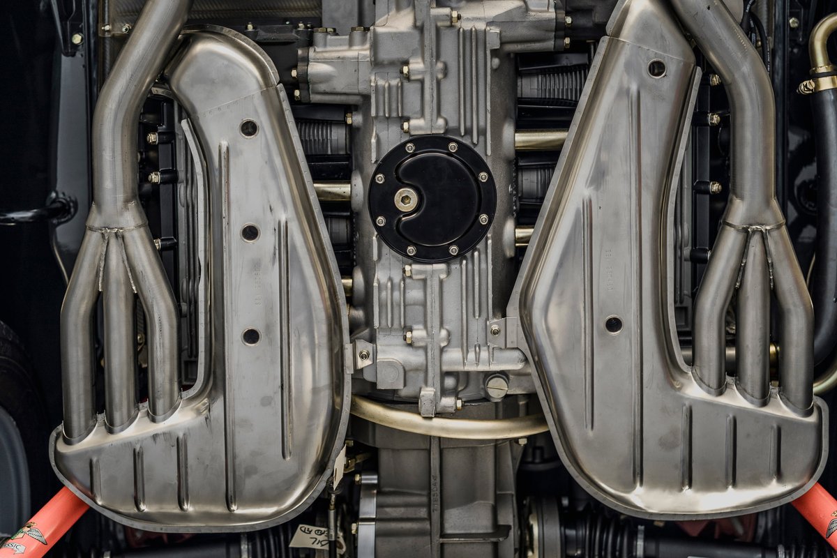 Detailed view of a black Porsche 911's air-cooled flat-six engine with polished stainless steel exhaust headers and heat exchangers.
