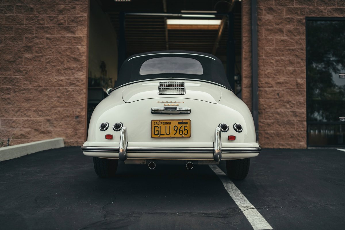 Iconic white Porsche 356 Cabriolet rear, with black soft top, chrome bumpers, engine lid grille, and CA 'GLU 965' plate.