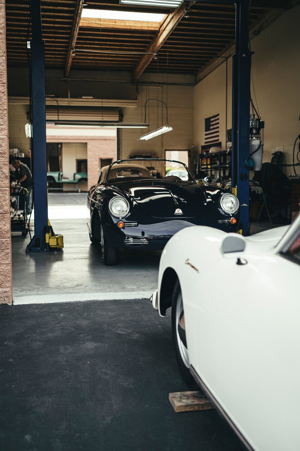 Dark blue Porsche 356 Speedster convertible, soft top down, featuring chrome trim and classic steel wheels, in a service garage.