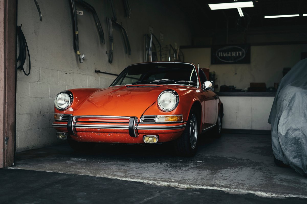 Vibrant orange classic Porsche 911 with chrome bumper trim, fog lights, and period wheels in a garage.