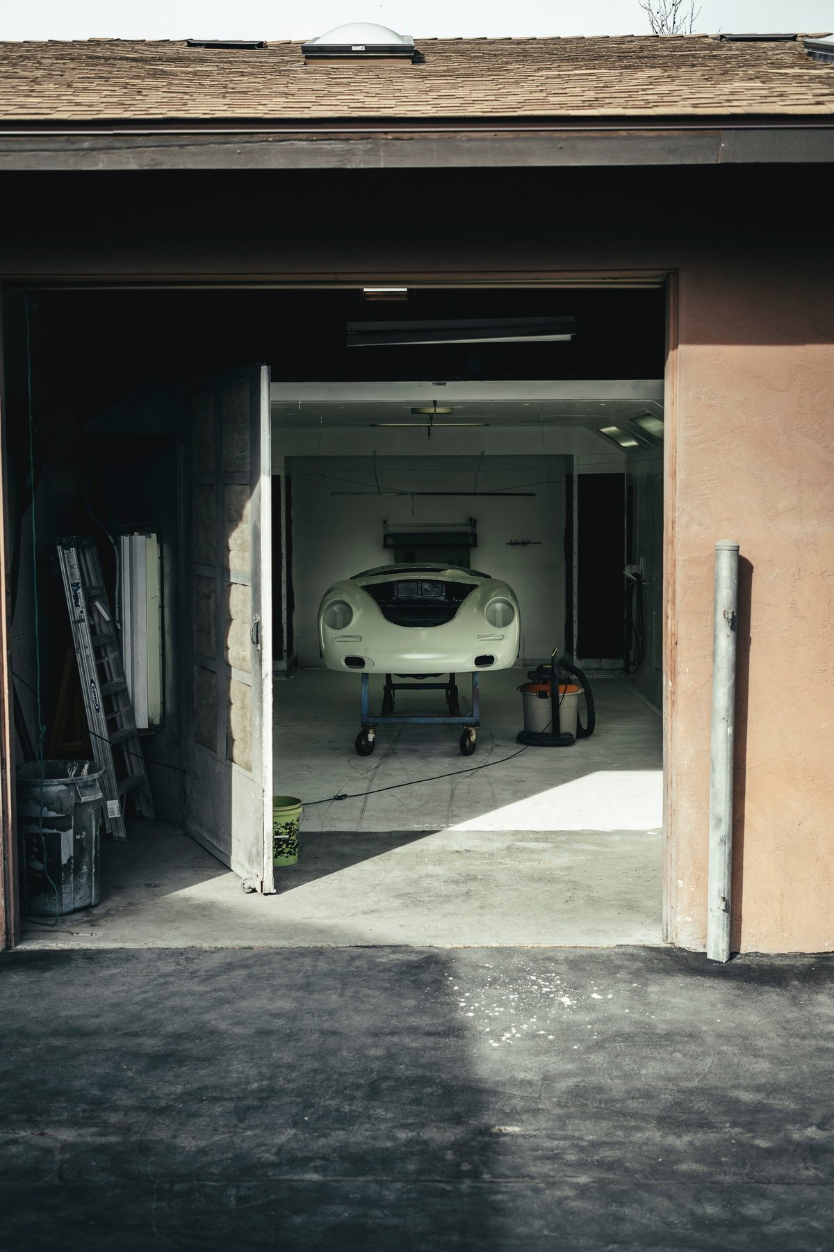 Front view of a creme white Porsche 356 body shell on a workshop cart, ready for restoration.