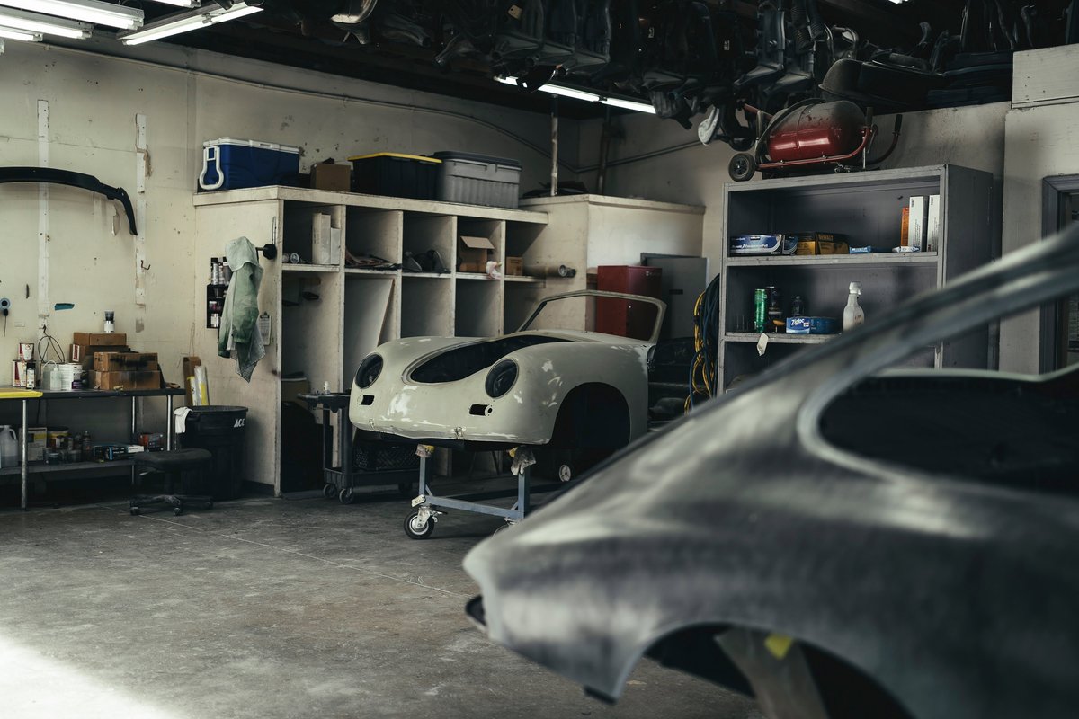 White Porsche 356 front clip in primer on a restoration dolly, alongside a raw metal classic Porsche body shell.