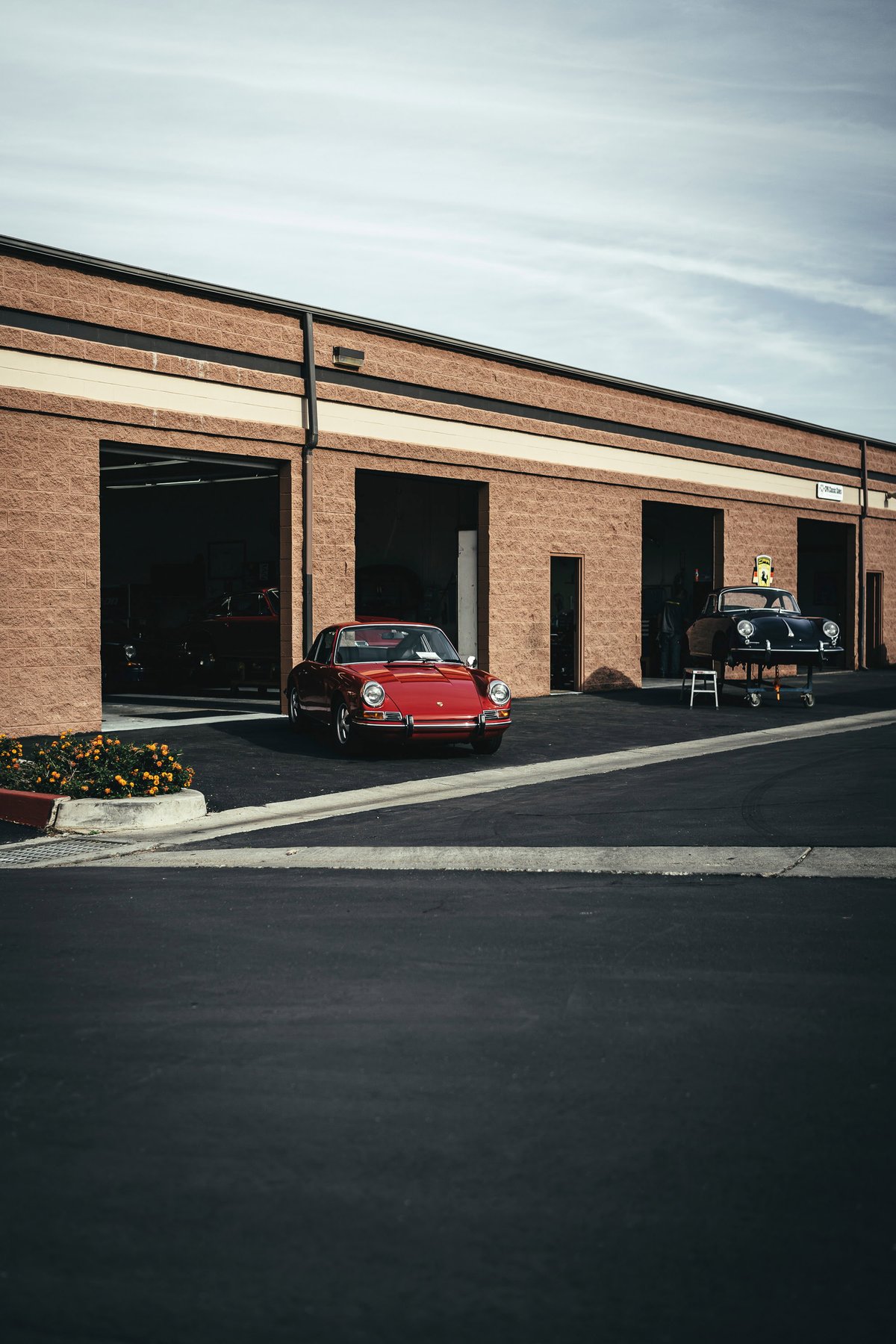 Vibrant red vintage Porsche 911, period-correct Fuchs-style wheels, parked outside a classic car restoration bay.
