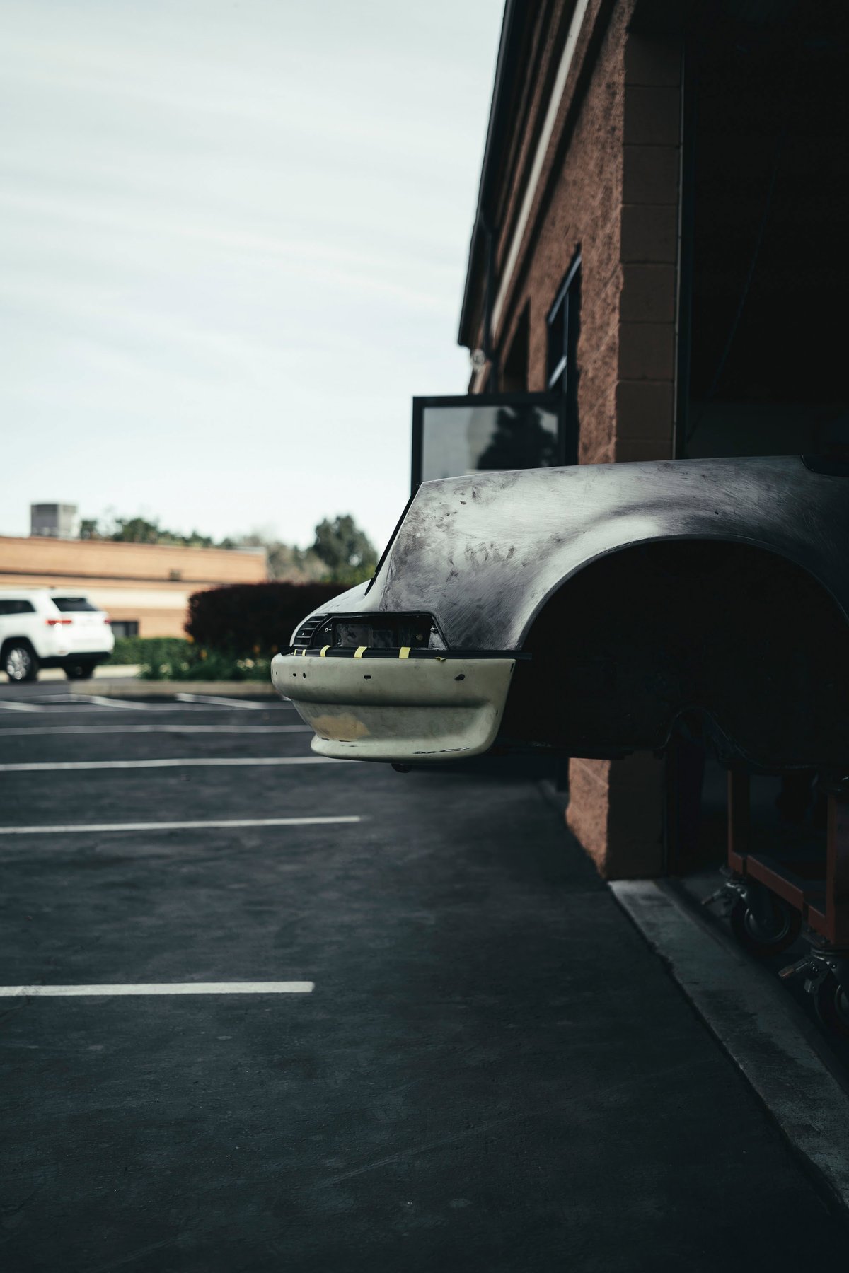 Air-cooled Porsche 911 front fender and bumper in bare metal and primer, undergoing custom restoration bodywork.