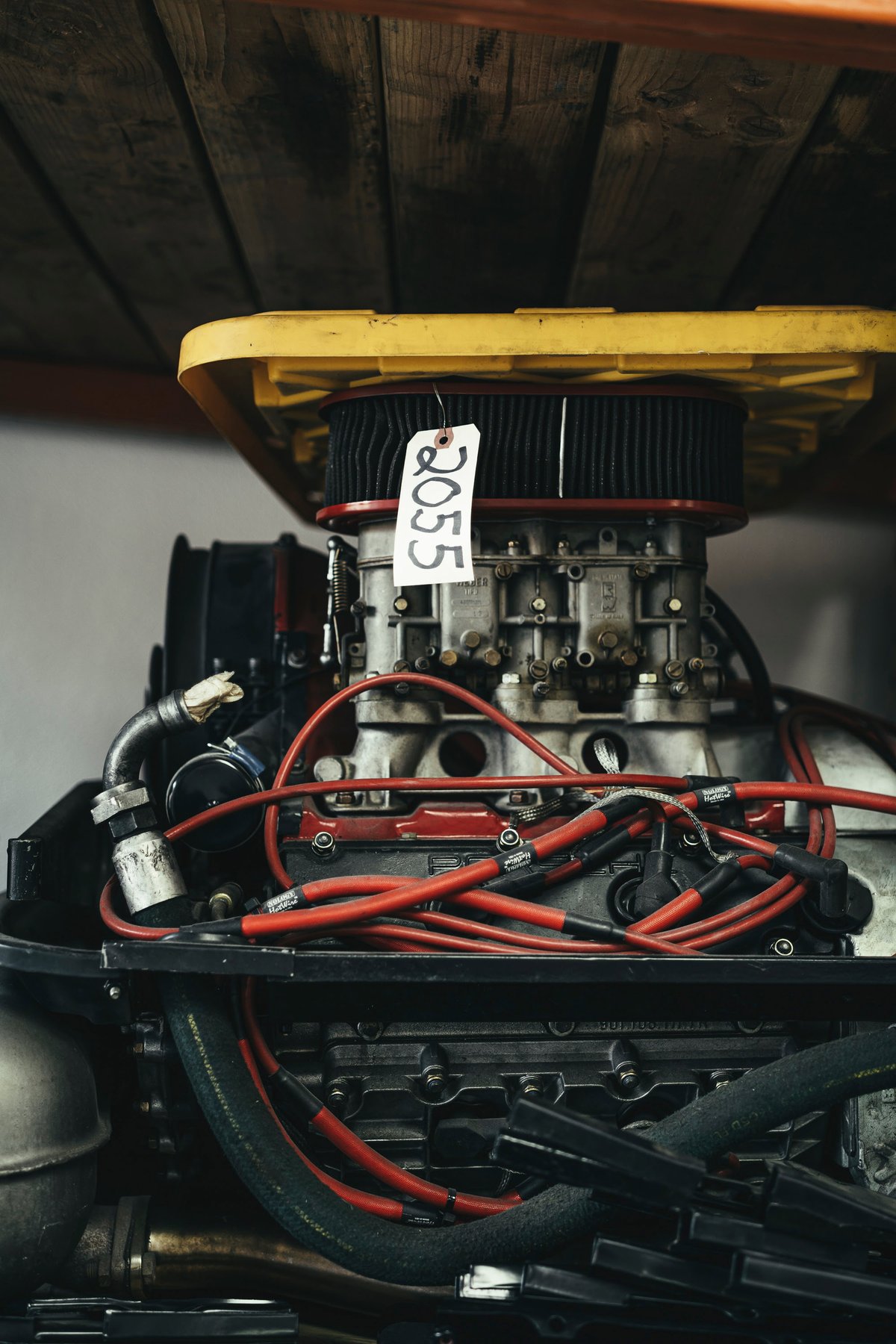 Close-up of a classic performance engine, featuring multiple side-draft carburetors, red ignition wires, and a black open-element air filter.
