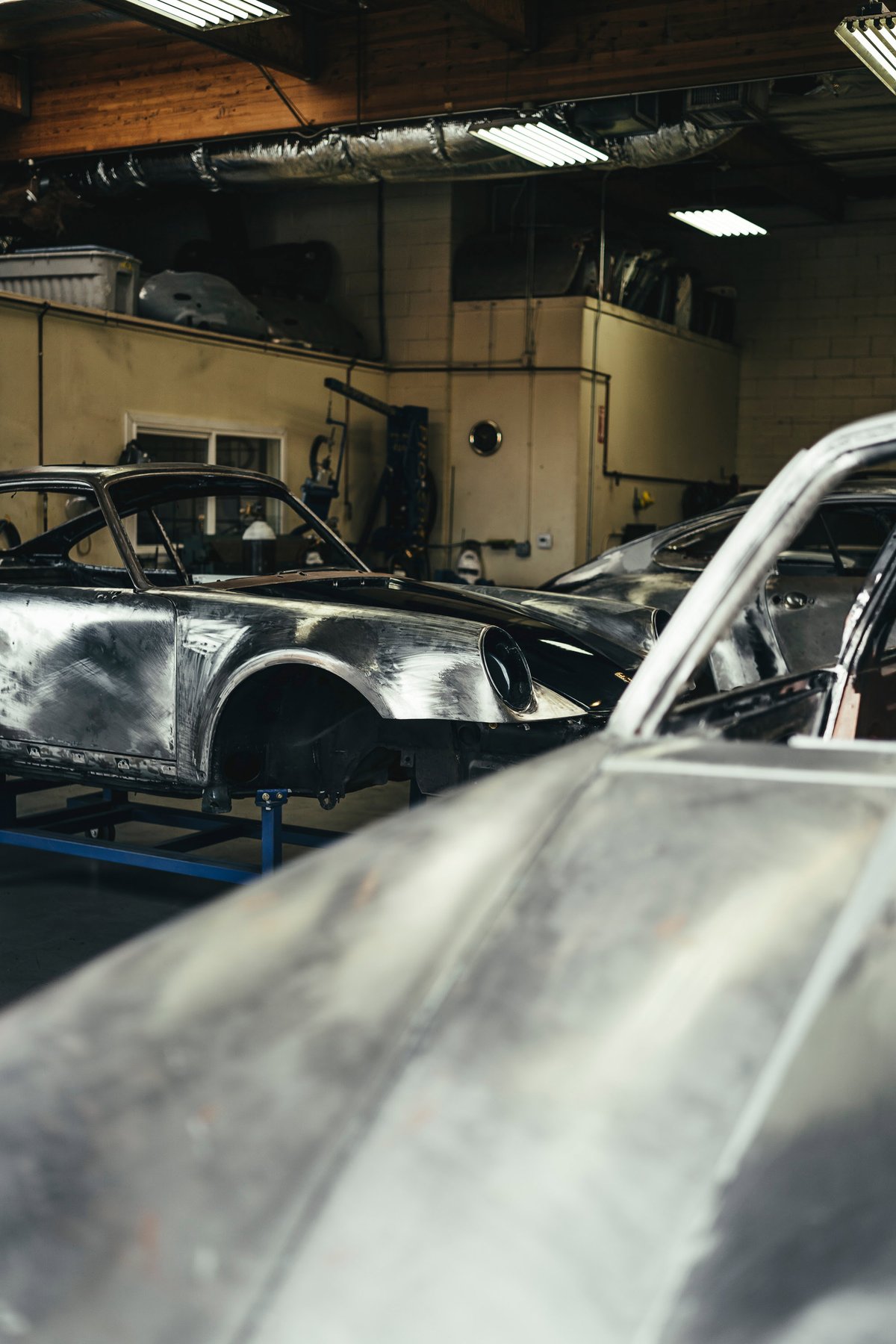 Bare metal classic Porsche 911 body, prepped for restoration or custom paint, on a jig in a Los Angeles workshop.