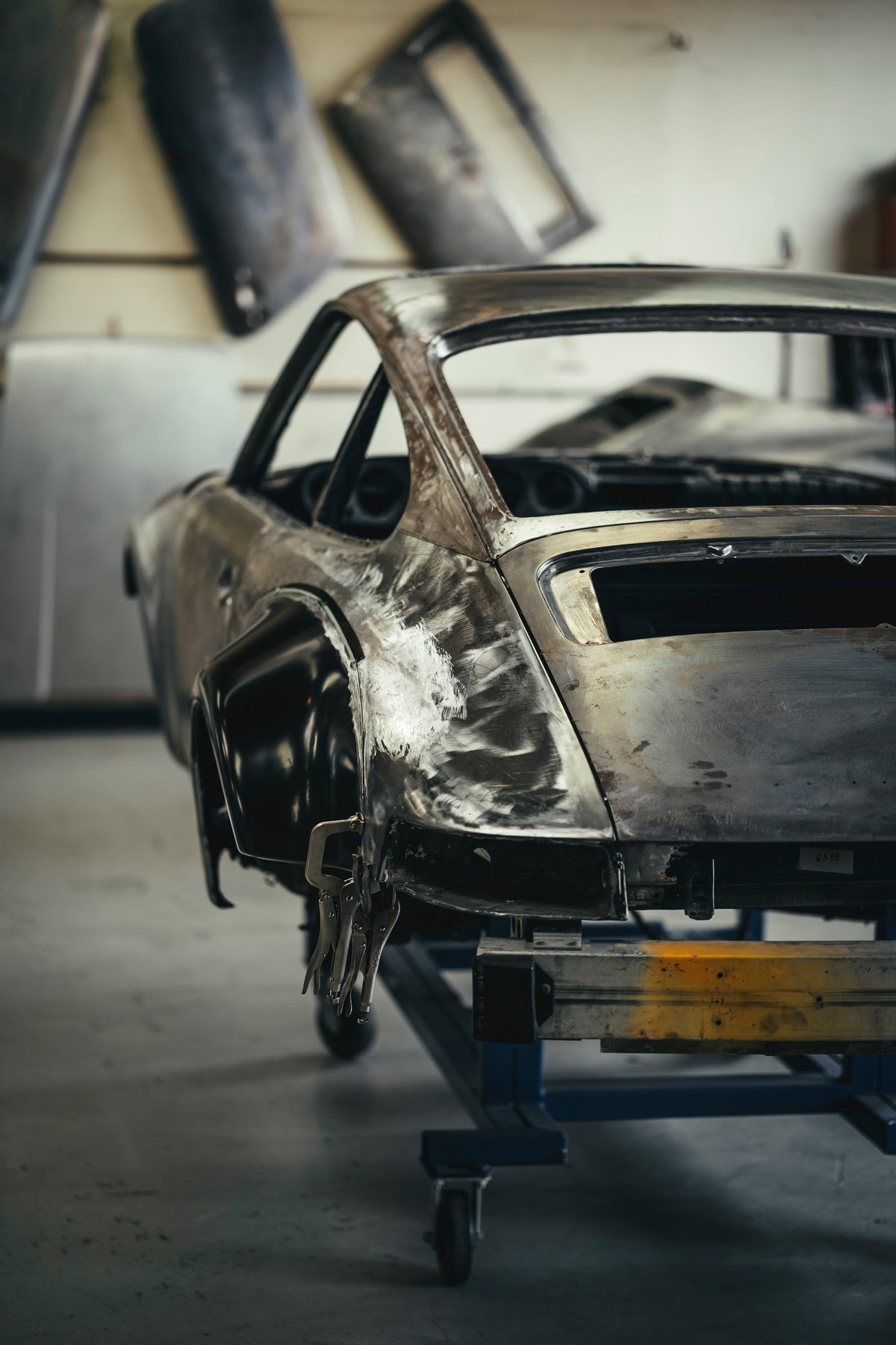 Classic Porsche 911 custom widebody build, bare metal shell on a chassis jig with RSR fender flares clamped.