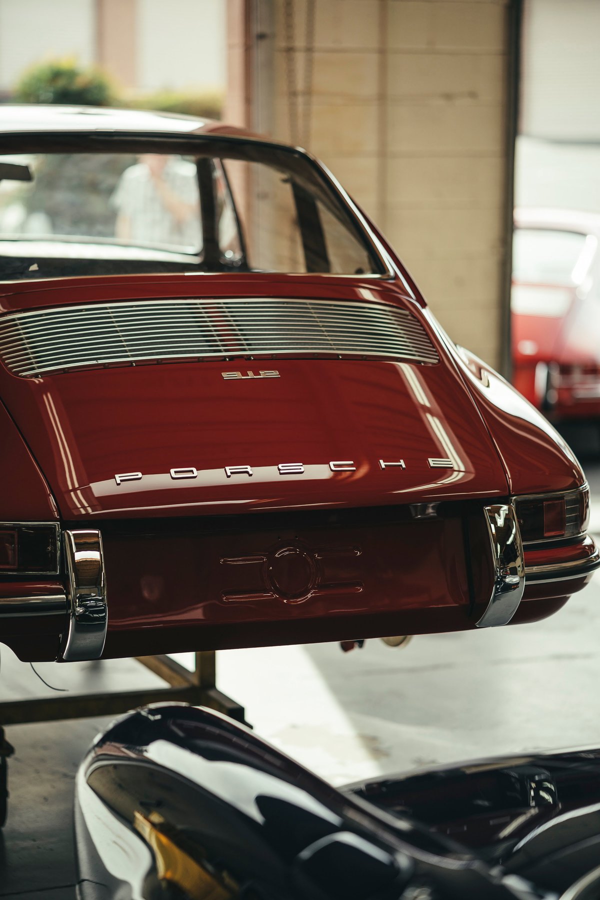Rear view of a pristine classic red Porsche 911, showcasing its iconic slatted engine lid grille, chrome bumperettes, and PORSCHE badging.