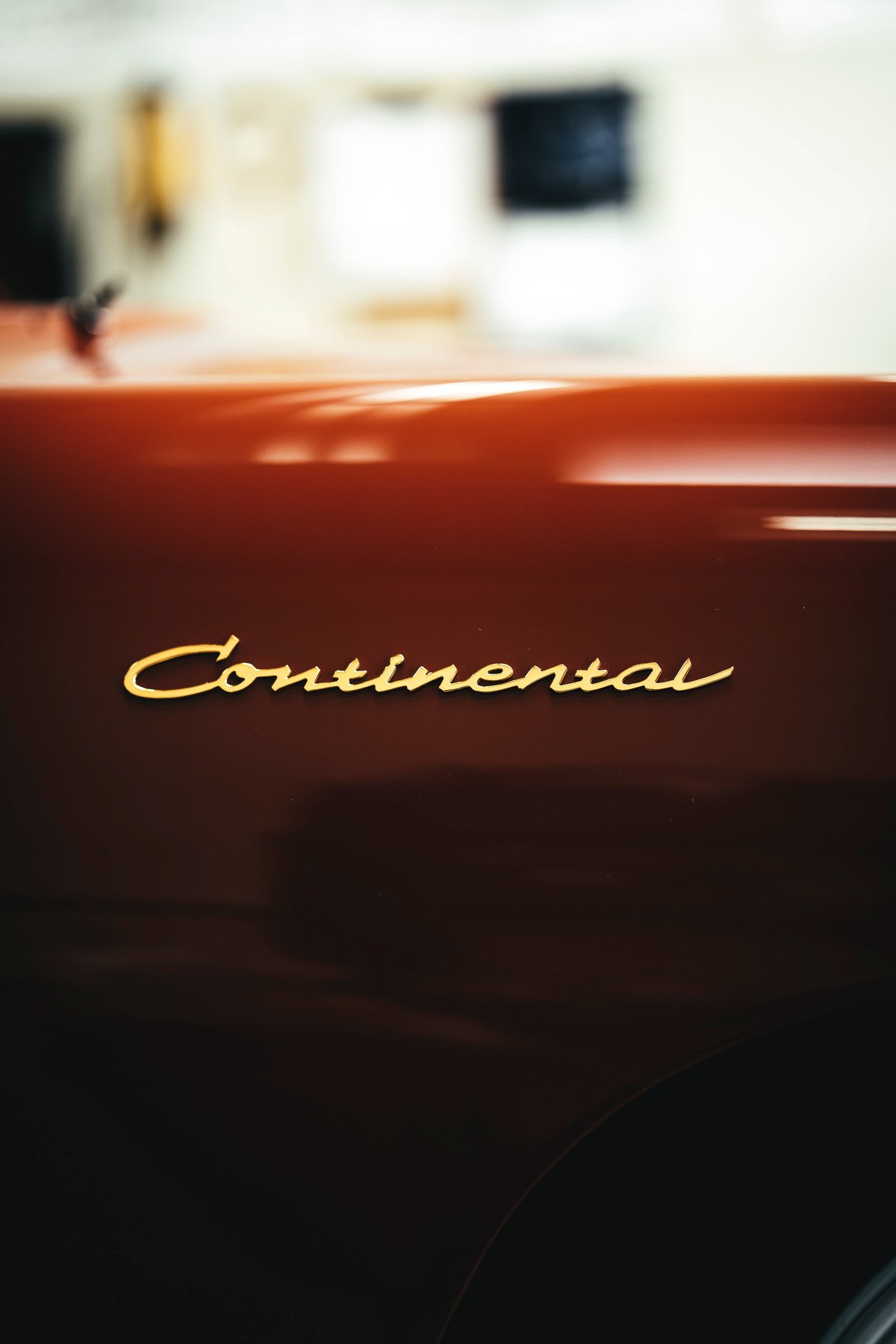 Gold 'Continental' script badging on a vintage Lincoln Continental's metallic bronze fender, reflecting light. Los Angeles.