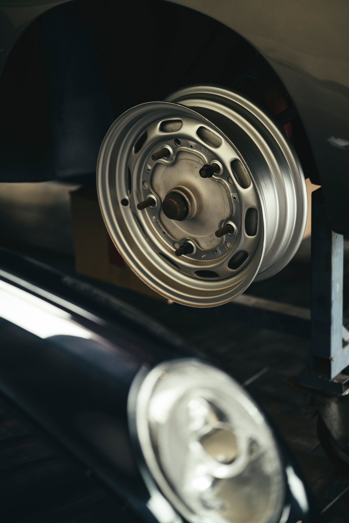 Bare polished Fuchs-style alloy rim on a classic Porsche 911's wheel hub. Visible studs, dark bodywork.