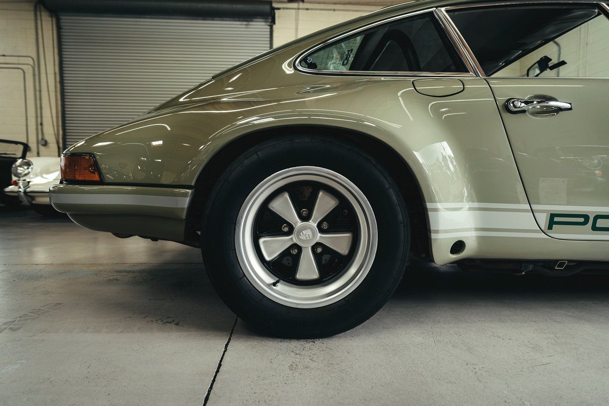 Classic light green Porsche 911 rear quarter, with white PORSCHE livery stripes, chrome door handle, and polished Fuchs wheels.