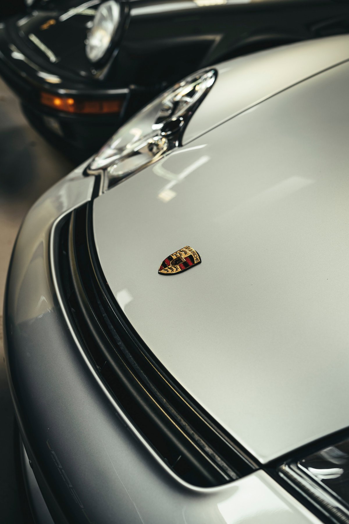 Silver Porsche 911 (991/992) front close-up: iconic hood crest, modern LED headlight, and sleek lower grille trim.