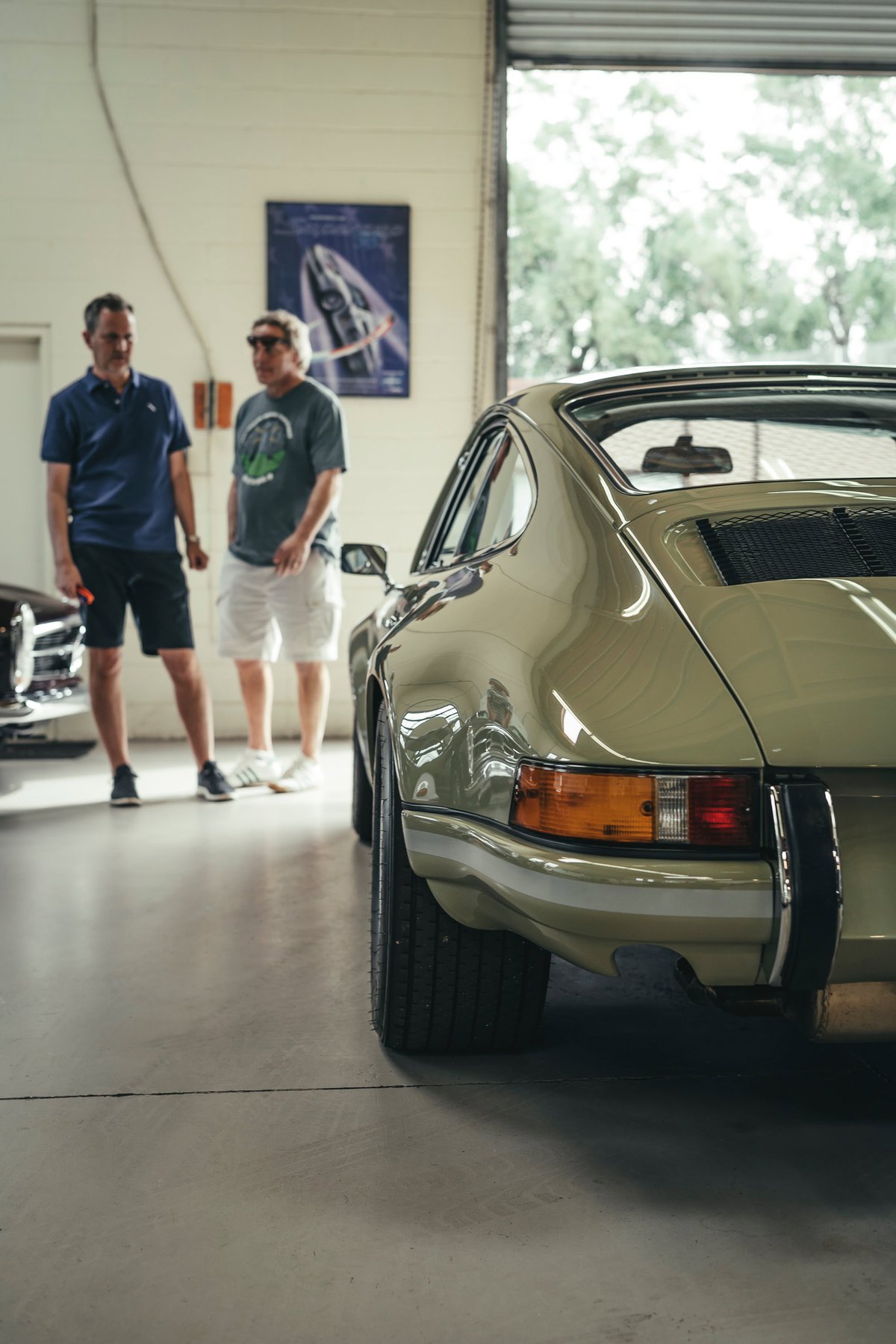 Sage green air-cooled Porsche 911 G-Series rear quarter view, with flared fenders, impact bumpers, and black engine grille.